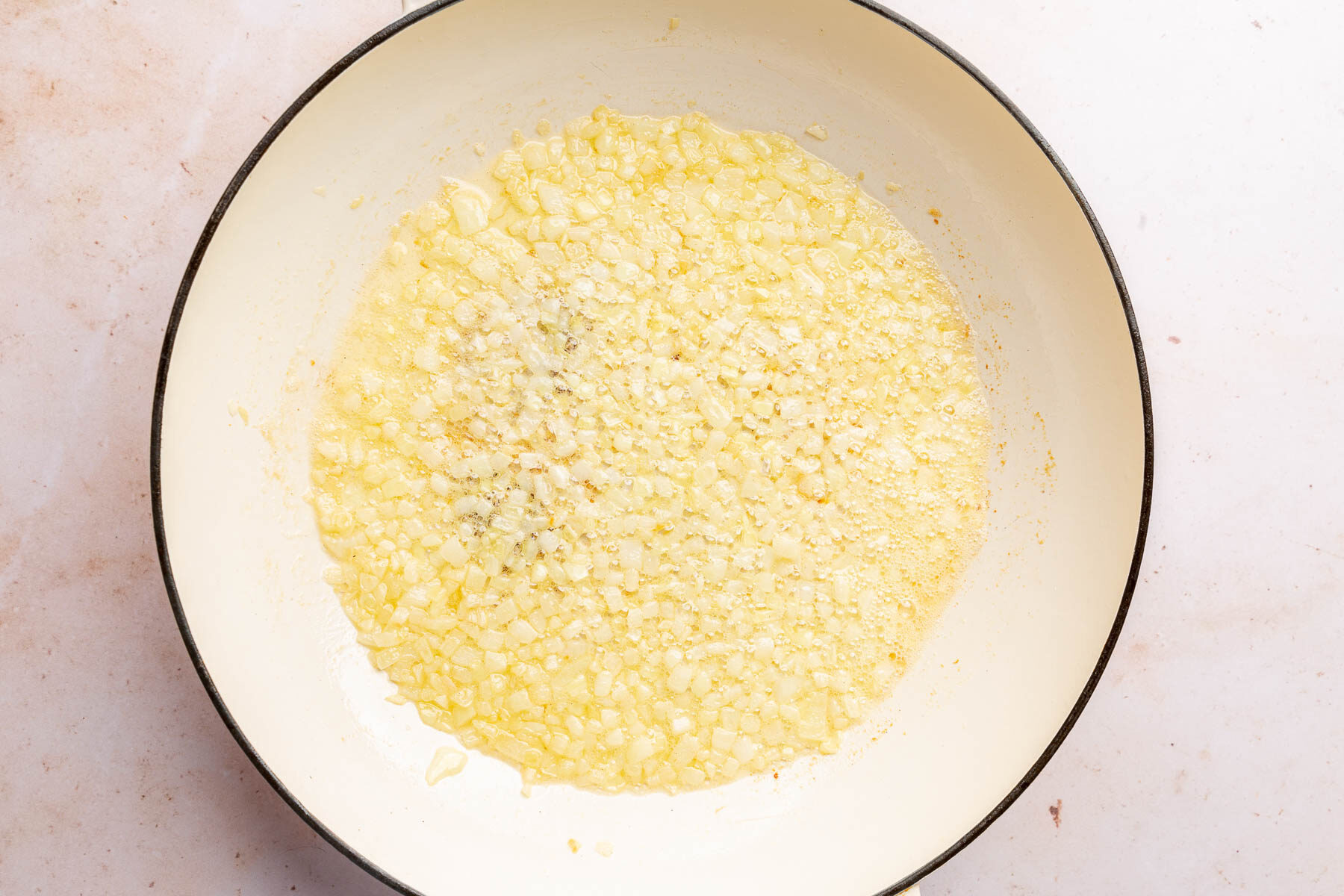 A braising pan with sautéed yellow onions in melted butter.