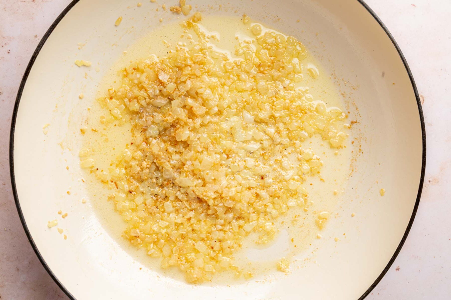 A braising pan with melted butter mixed together with sautéed yellow onions and minced garlic.