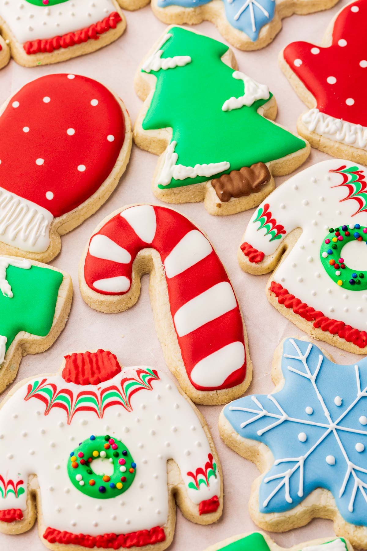 A close up of gluten free Christmas cut-out sugar cookies decorated as ugly Christmas sweaters, snowflakes, Christmas trees, candy canes and polka dot mittens.