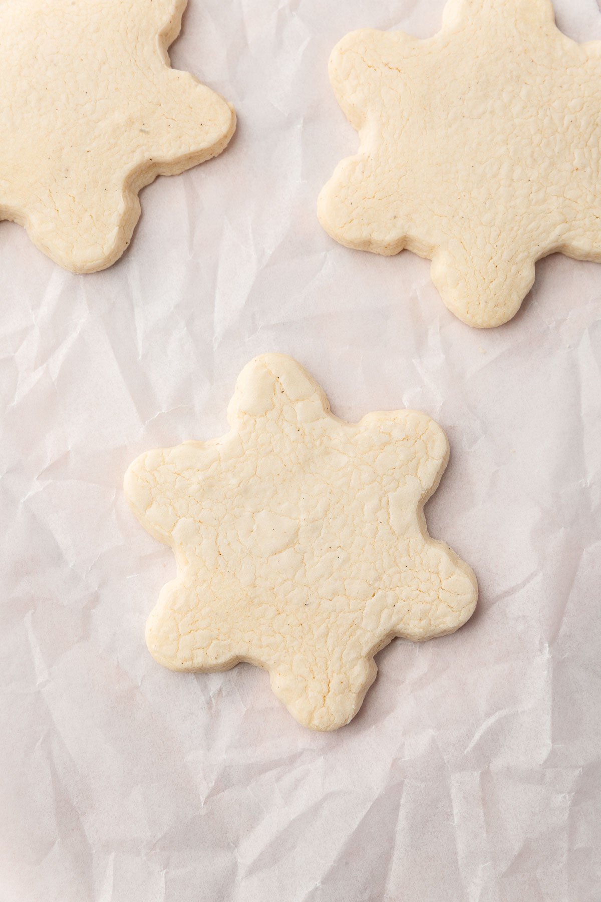 Three gluten-free snowflake cookies on a piece of parchment paper.