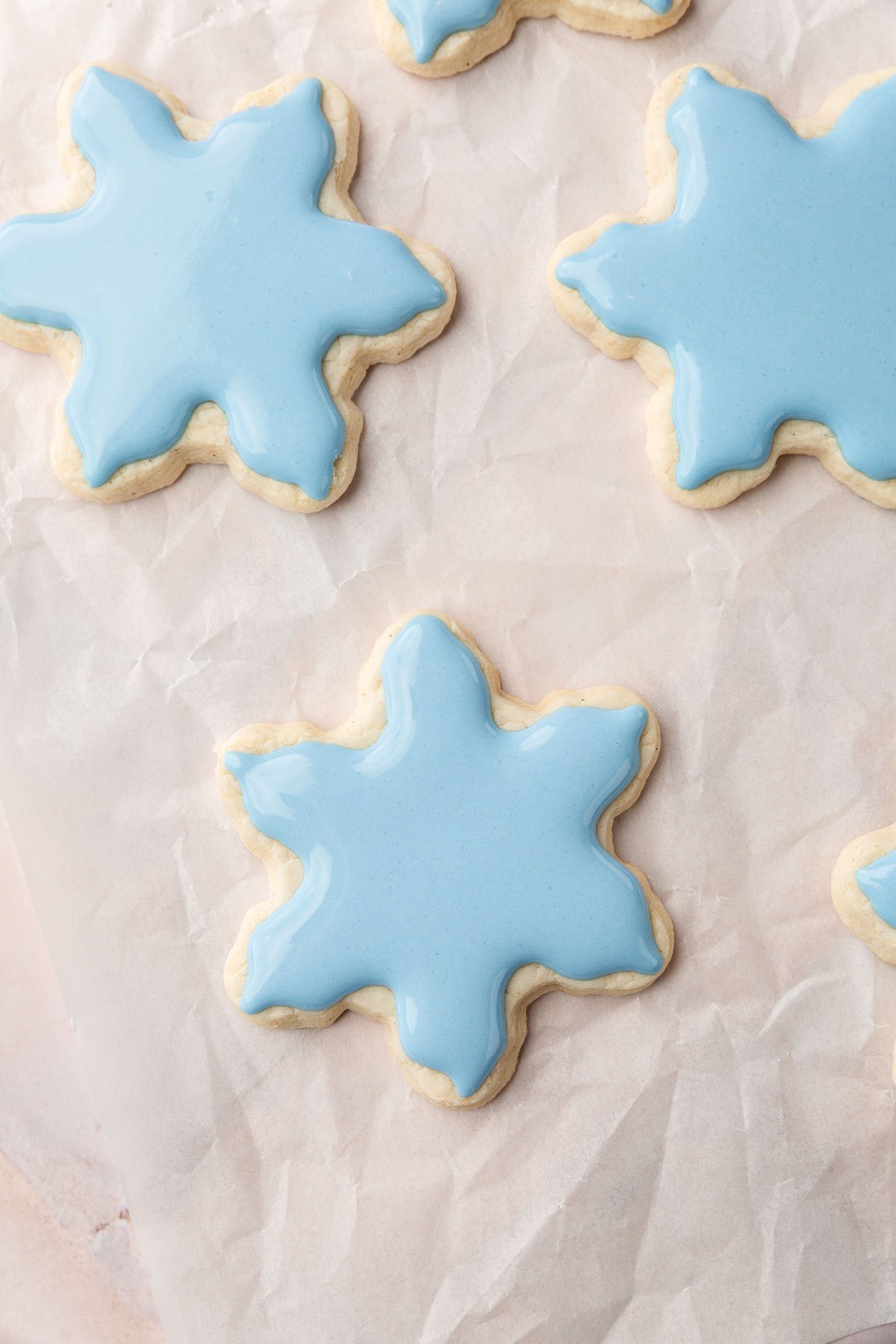 Three gluten-free snowflake cookies frosted with blue royal icing on a piece of parchment paper.