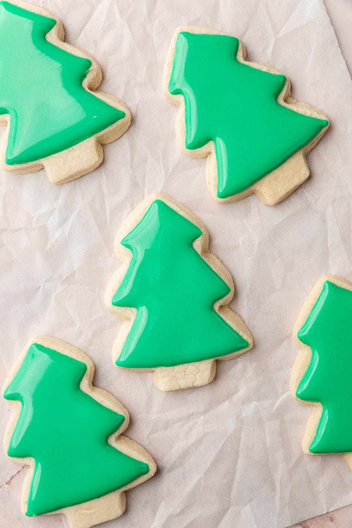 Multiple gluten-free Christmas tree sugar cookies iced with green royal icing on a piece of parchment paper.