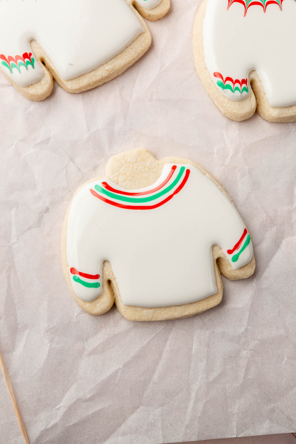 A few gluten free ugly sweater Christmas cookies on a piece of parchment paper with one decorated with white royal icing with a few red and green stripes.