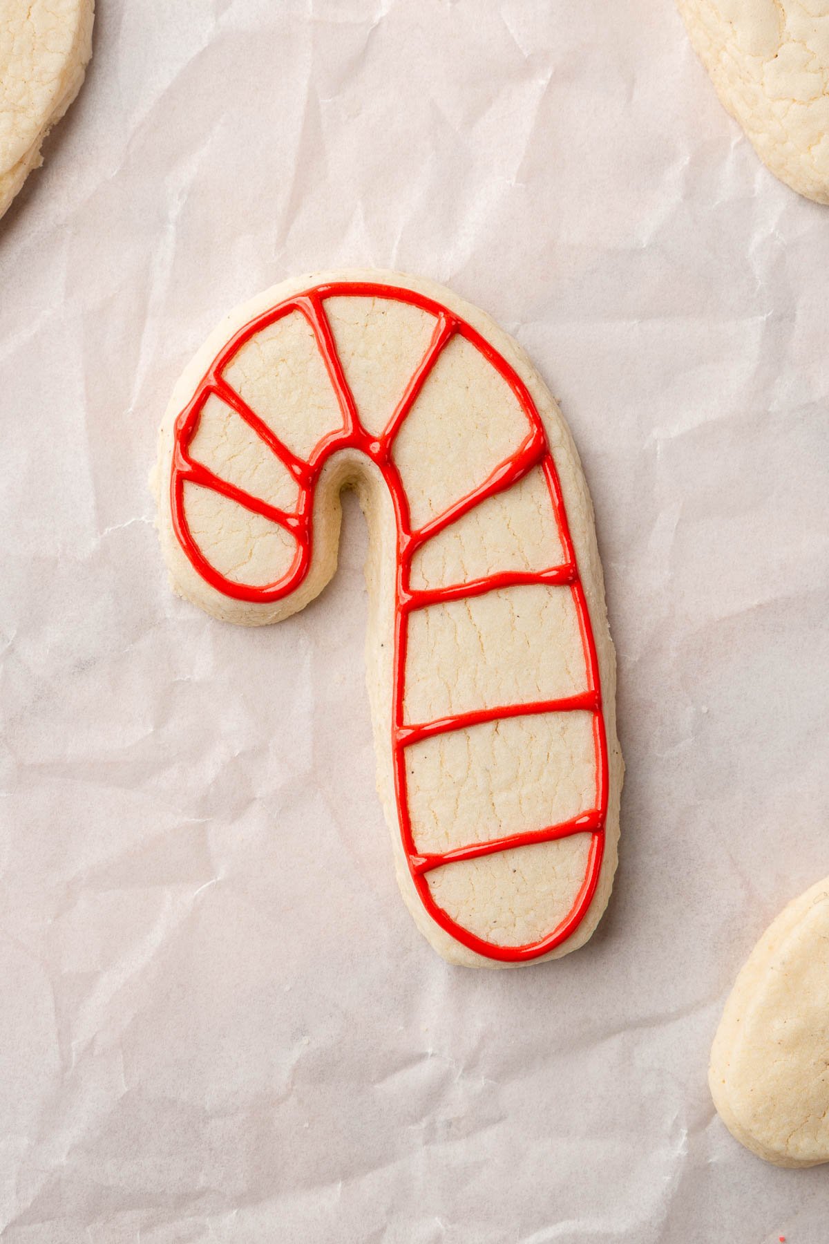 A few gluten free candy cane sugar cookies on a piece of parchment paper with one outlined in red royal icing.
