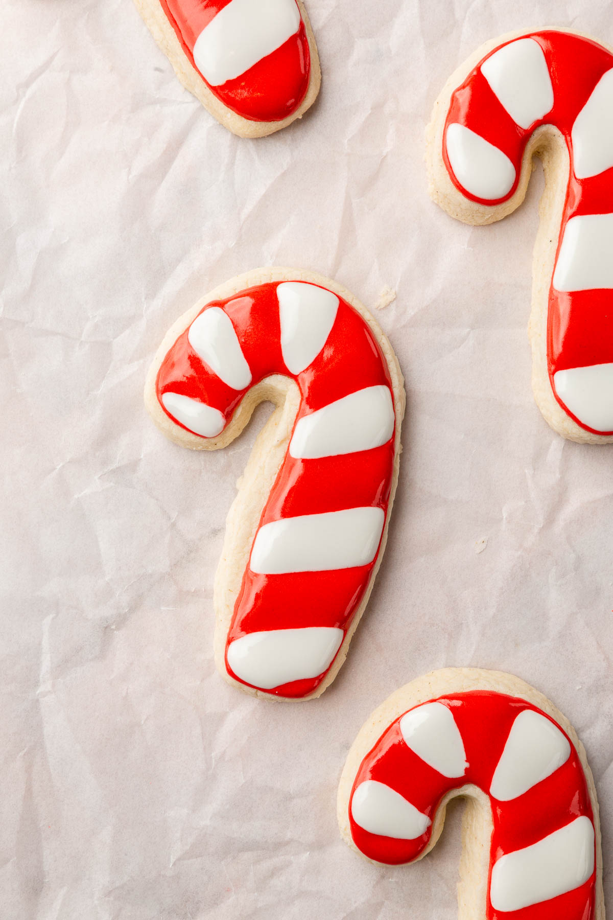A few gluten free candy cane sugar cookies on a piece of parchment paper decorated with red and white royal icing stripes.