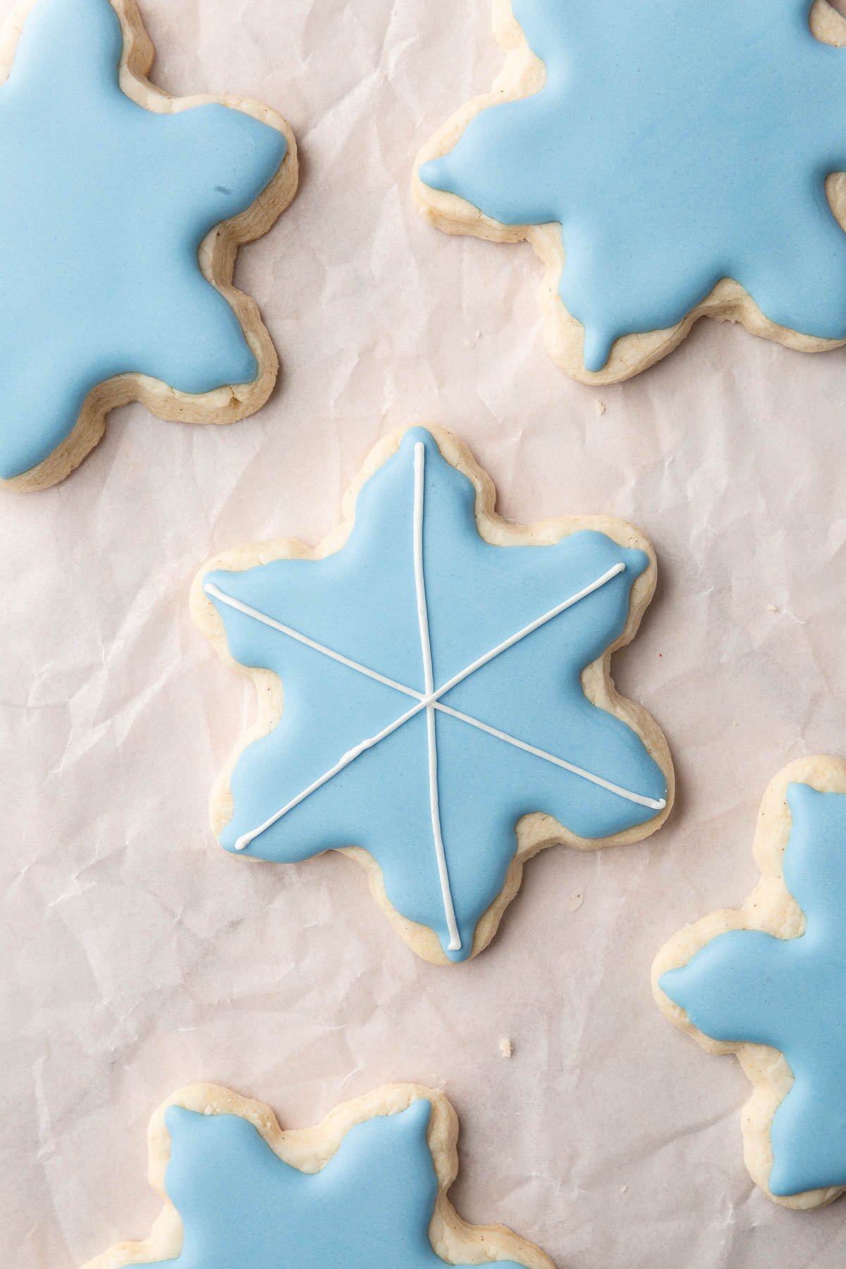 A few gluten-free snowflake sugar cookies decorated with blue royal icing with one having white royal icing stripes on top.