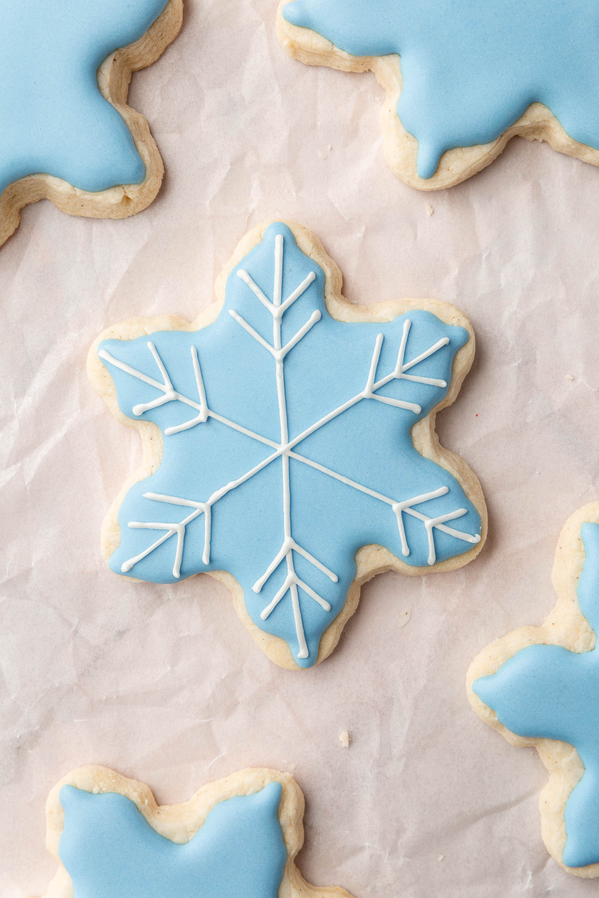 A few gluten-free snowflake sugar cookies decorated with blue royal icing with one having white royal icing details on top.