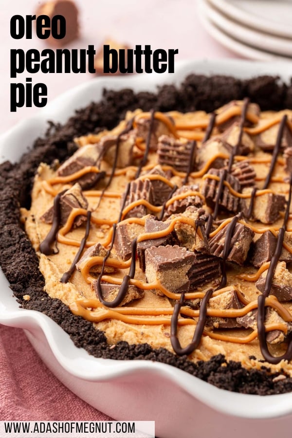 A whole gluten-free chocolate peanut butter pie with Oreo crust and topped with reese's peanut butter cups with a stack of plates in the background.