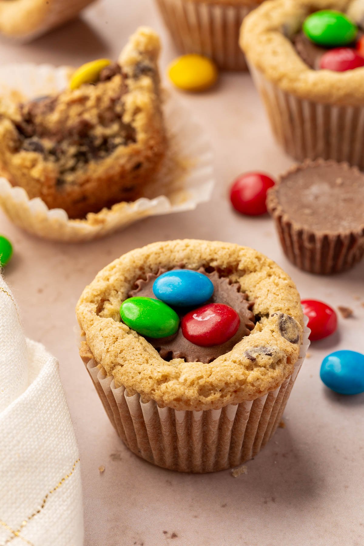 Chocolate chip cookie cup with a mini peanut butter cup inserted into the center and topped with three M&Ms.