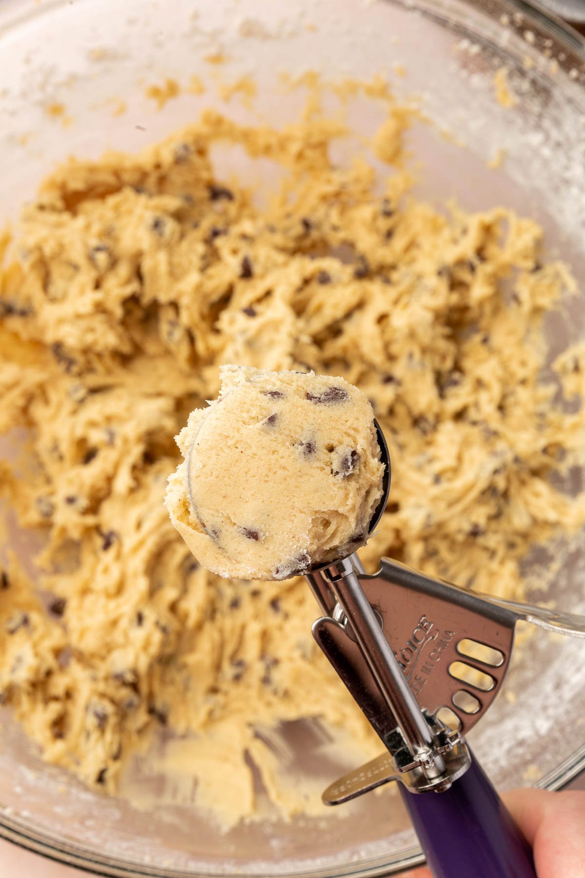 A portion scoop of gluten-free chocolate chip cookie dough over a mixing bowl of additional cookie dough.