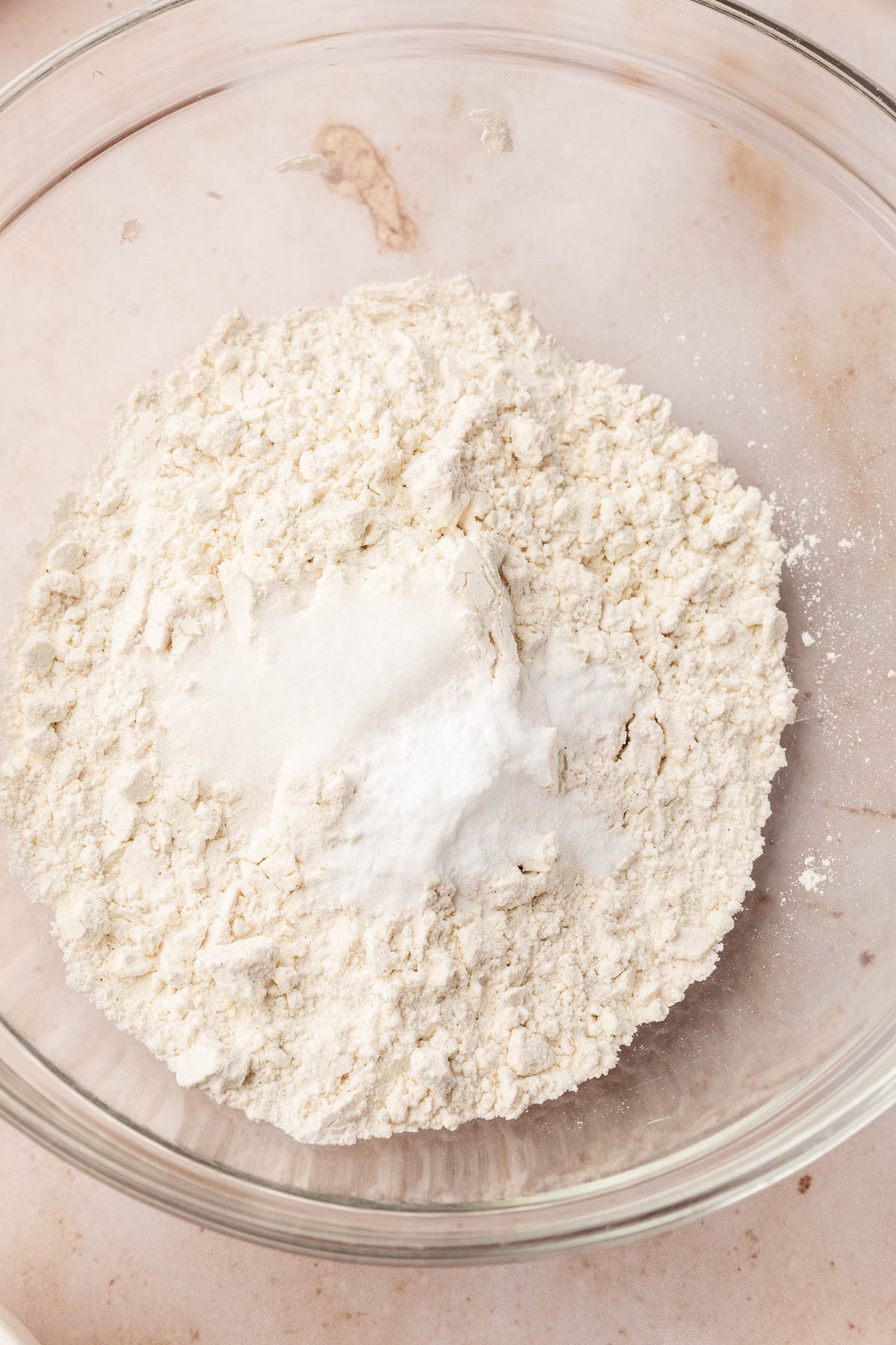 A glass mixing bowl of gluten-free flour topped with baking soda and salt before whisking together.
