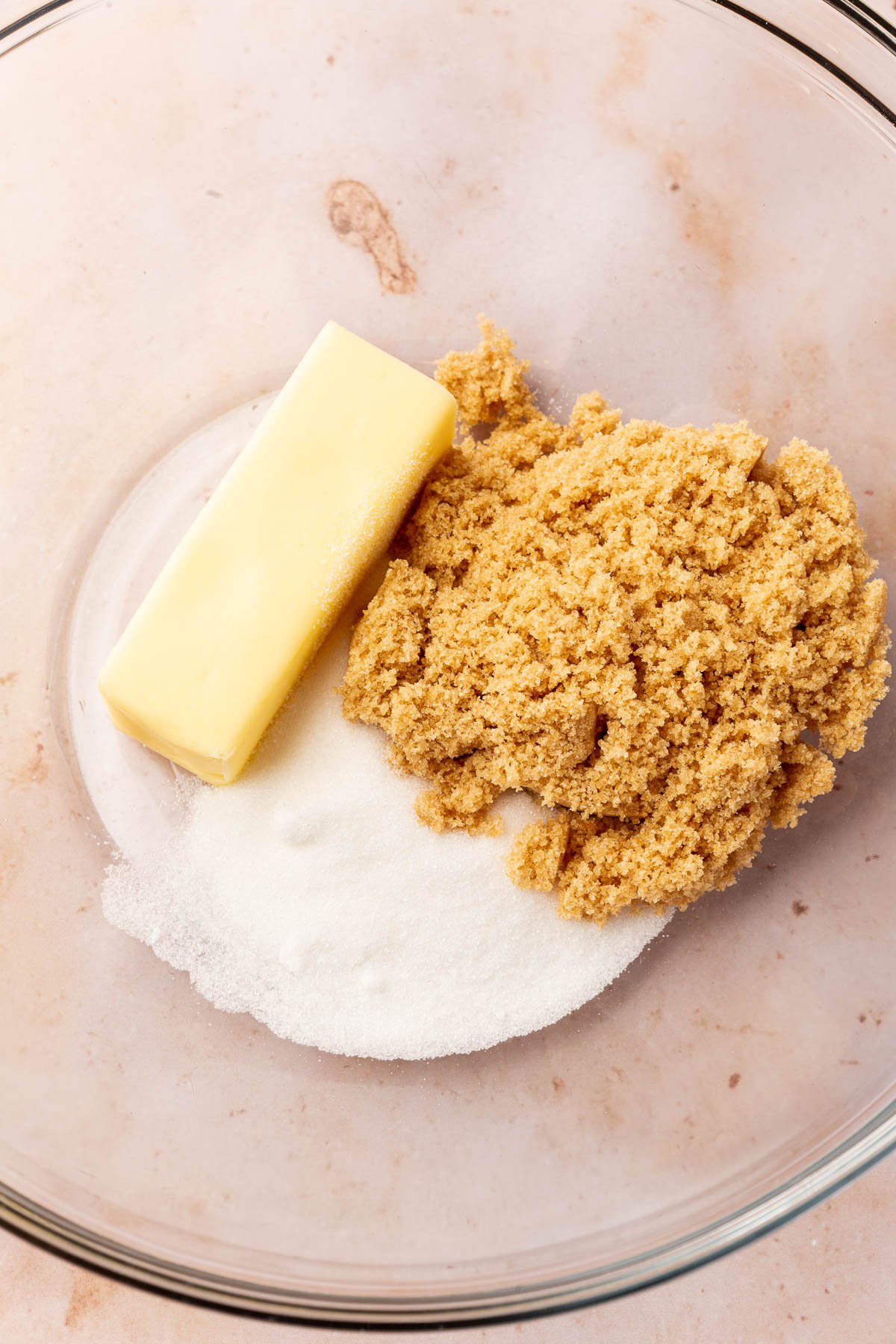 A glass mixing bowl with brown sugar, granulated sugar and a stick of softened butter.