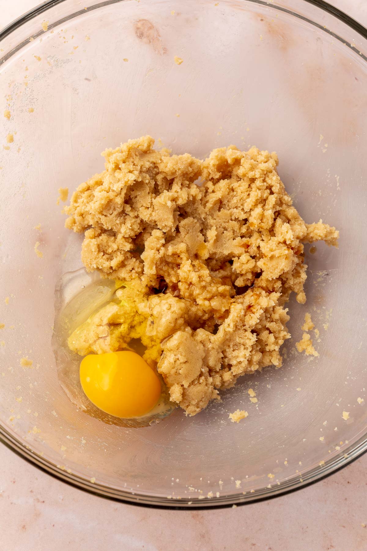 A glass mixing bowl of a creamed butter and brown sugar mixture next to a raw egg before mixing together.
