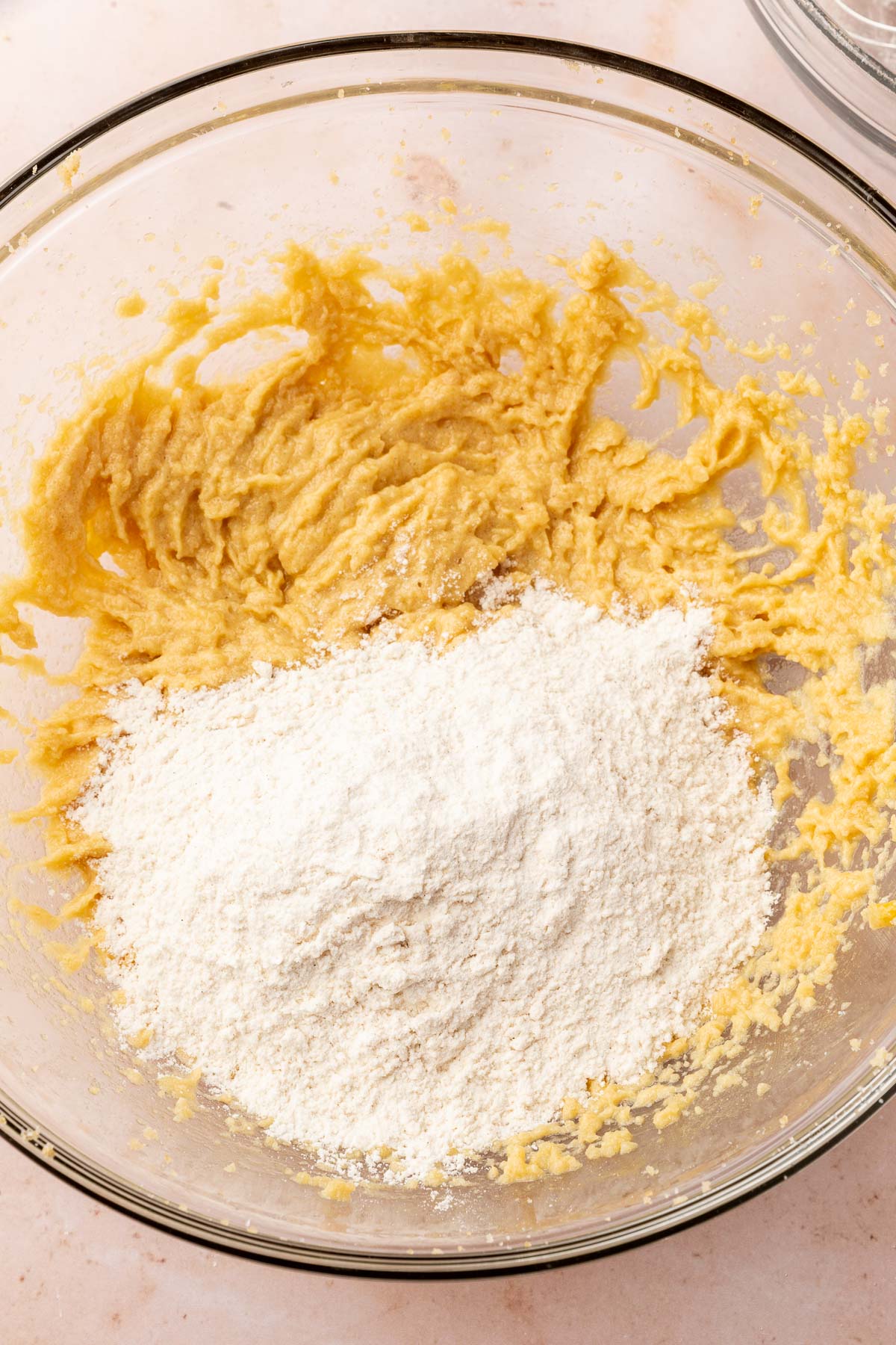 A glass mixing bowl of gluten-free cookie dough mixture topped with gluten-free flour before mixing together.