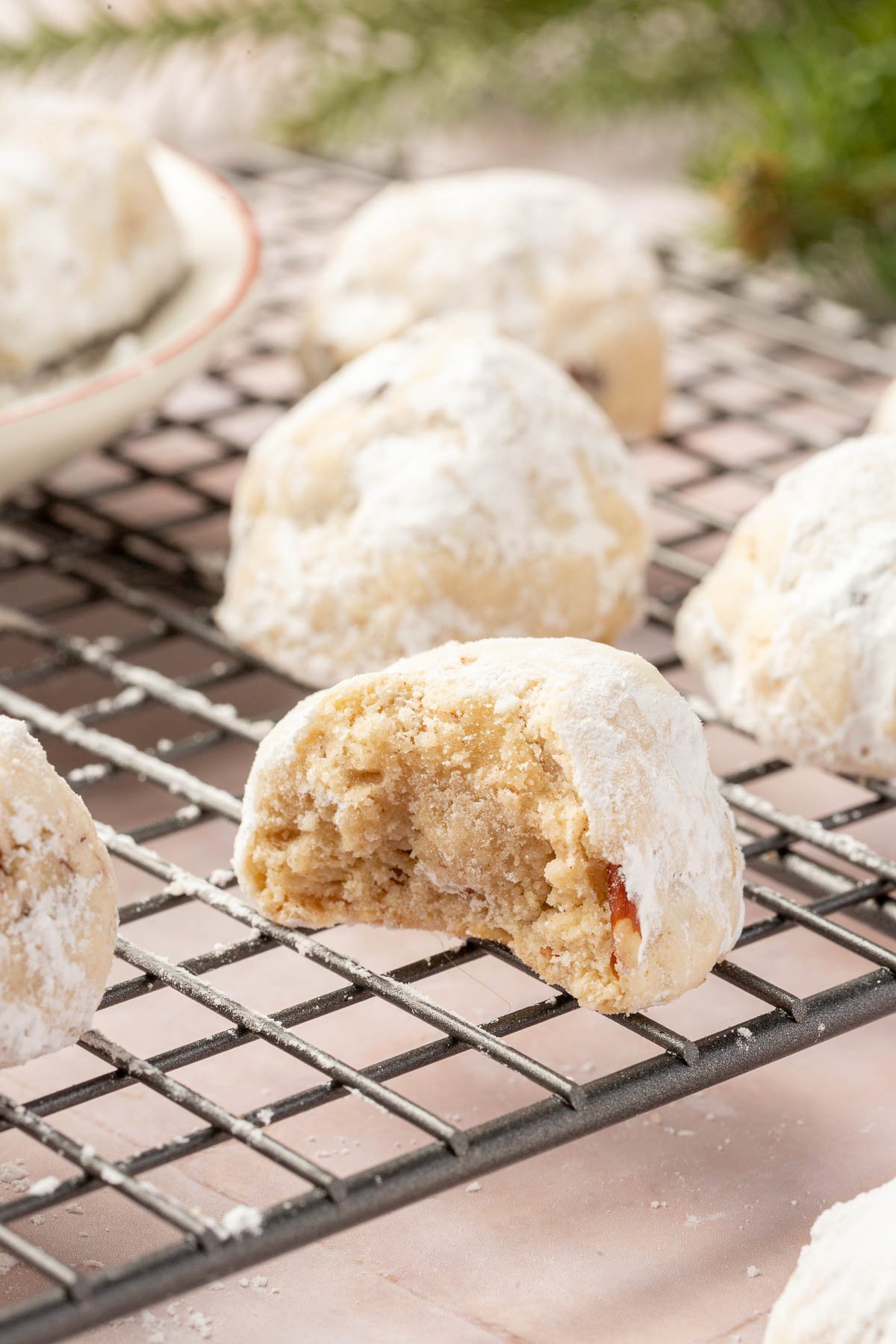 Gluten free snowball cookies dusted in powdered sugar on a cooling rack with the front cookie having a bite taken out of it.