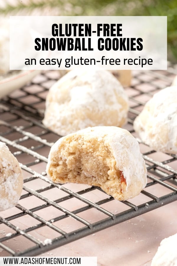 Gluten free snowball cookies dusted in powdered sugar on a cooling rack with the front cookie having a bite taken out of it.
