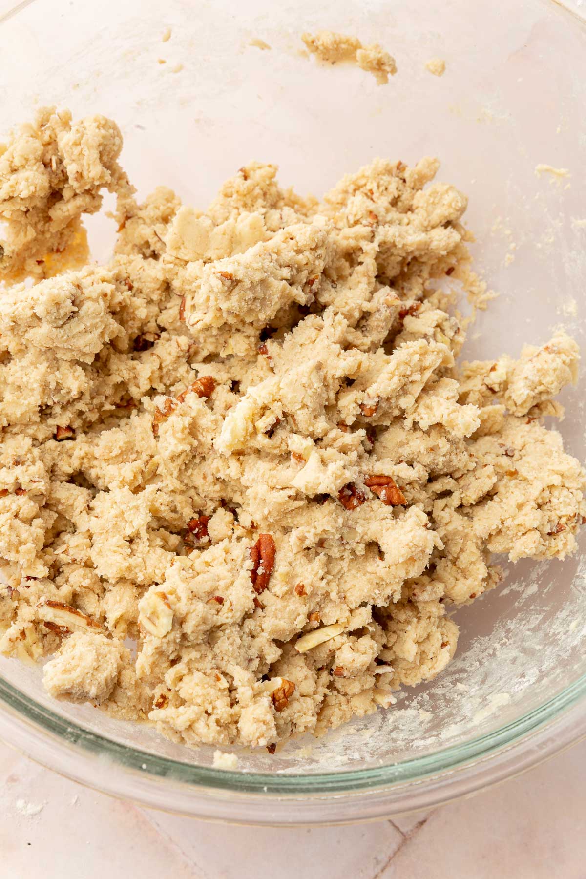 A glass mixing bowl with a gluten free snowball cookie dough with pecans in it.