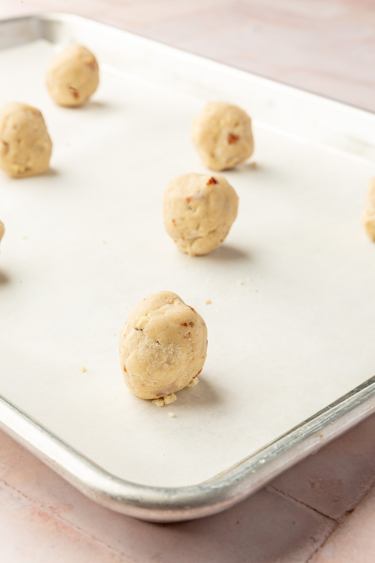 A baking sheet lined with parchment paper and topped with 9 gluten free snowball cookie dough balls before baking in the oven.