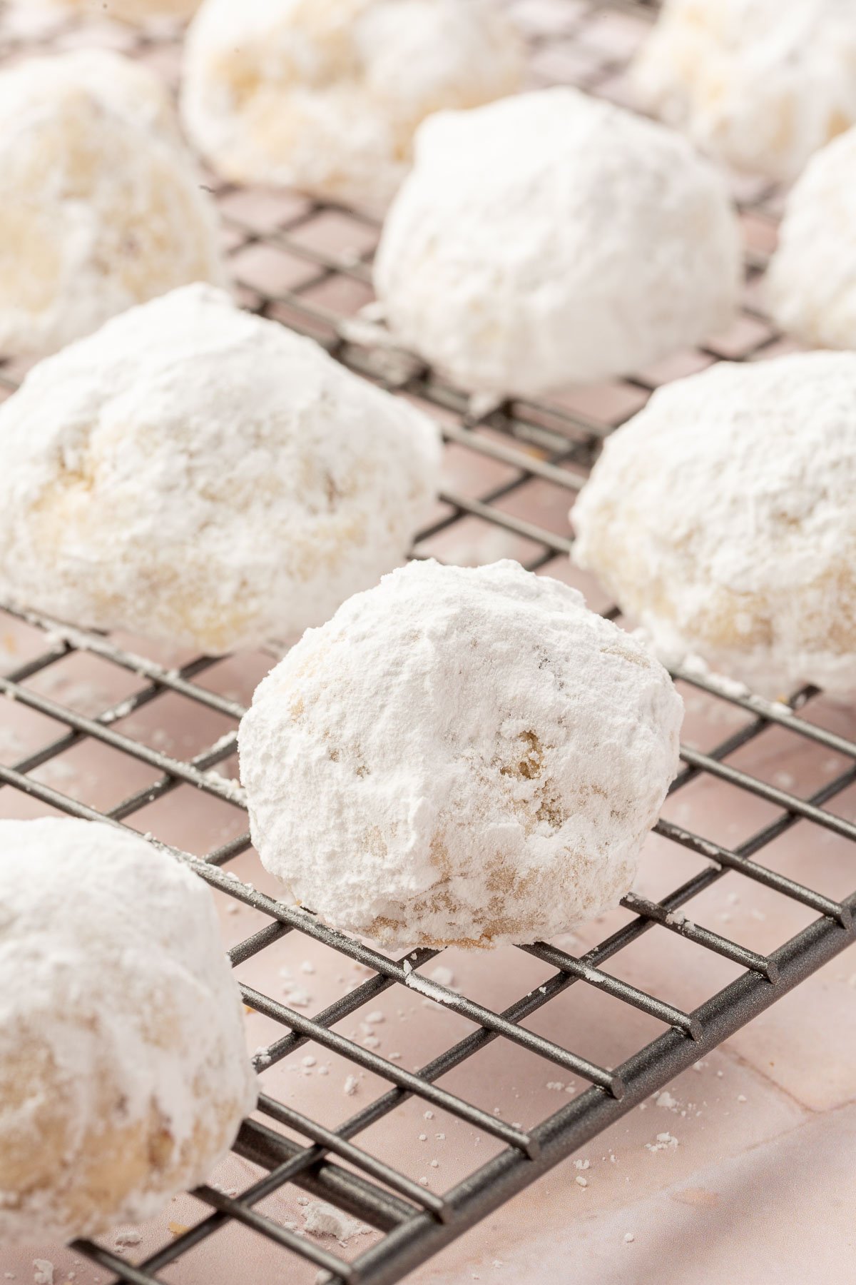 A wire cooling rack with snowball cookies on it that have been double coated in powdered sugar.