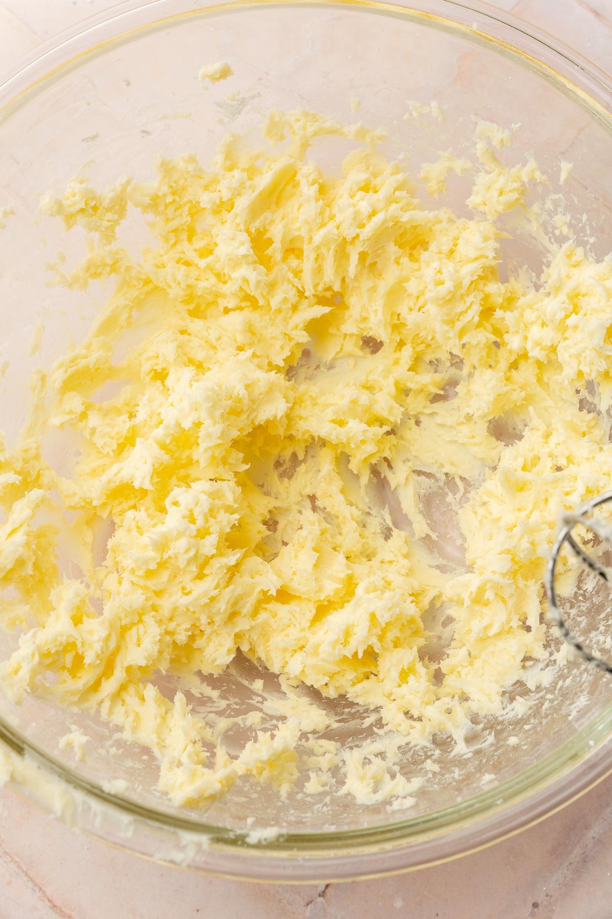 A glass mixing bowl with a mixture of creamed butter and powdered sugar in it.