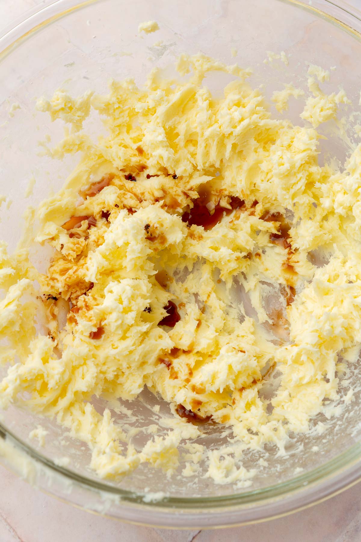 A glass mixing bowl with a mixture of creamed butter and powdered sugar in it topped with vanilla extract.