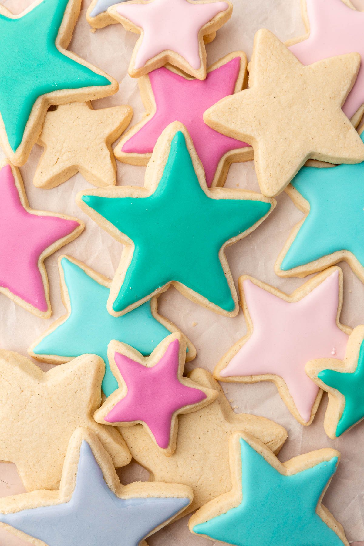 An overhead view of decorated and undecorated gluten free sugar cookies shaped as stars, some with blue, green, fuchsia and light pink icing.