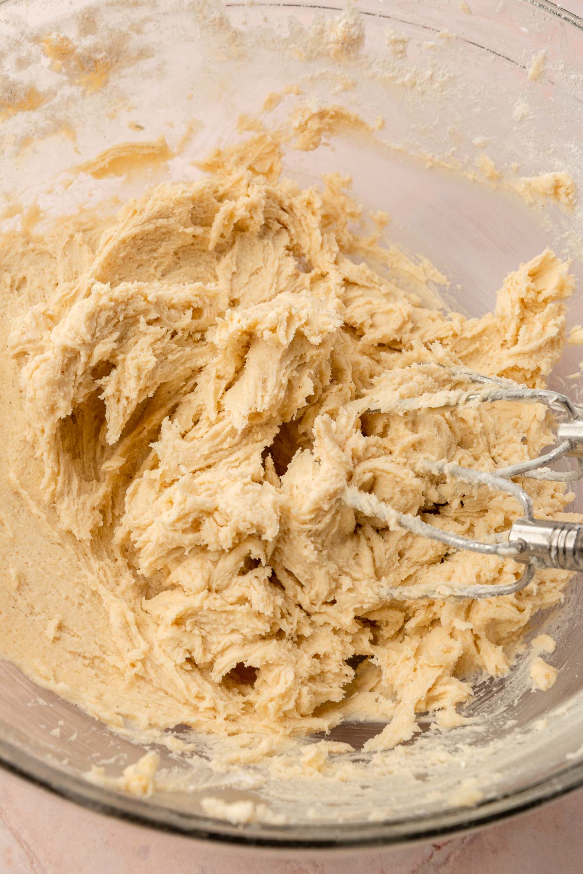 A glass mixing bowl with gluten-free sugar cookie dough in it with an electric mixer in it.