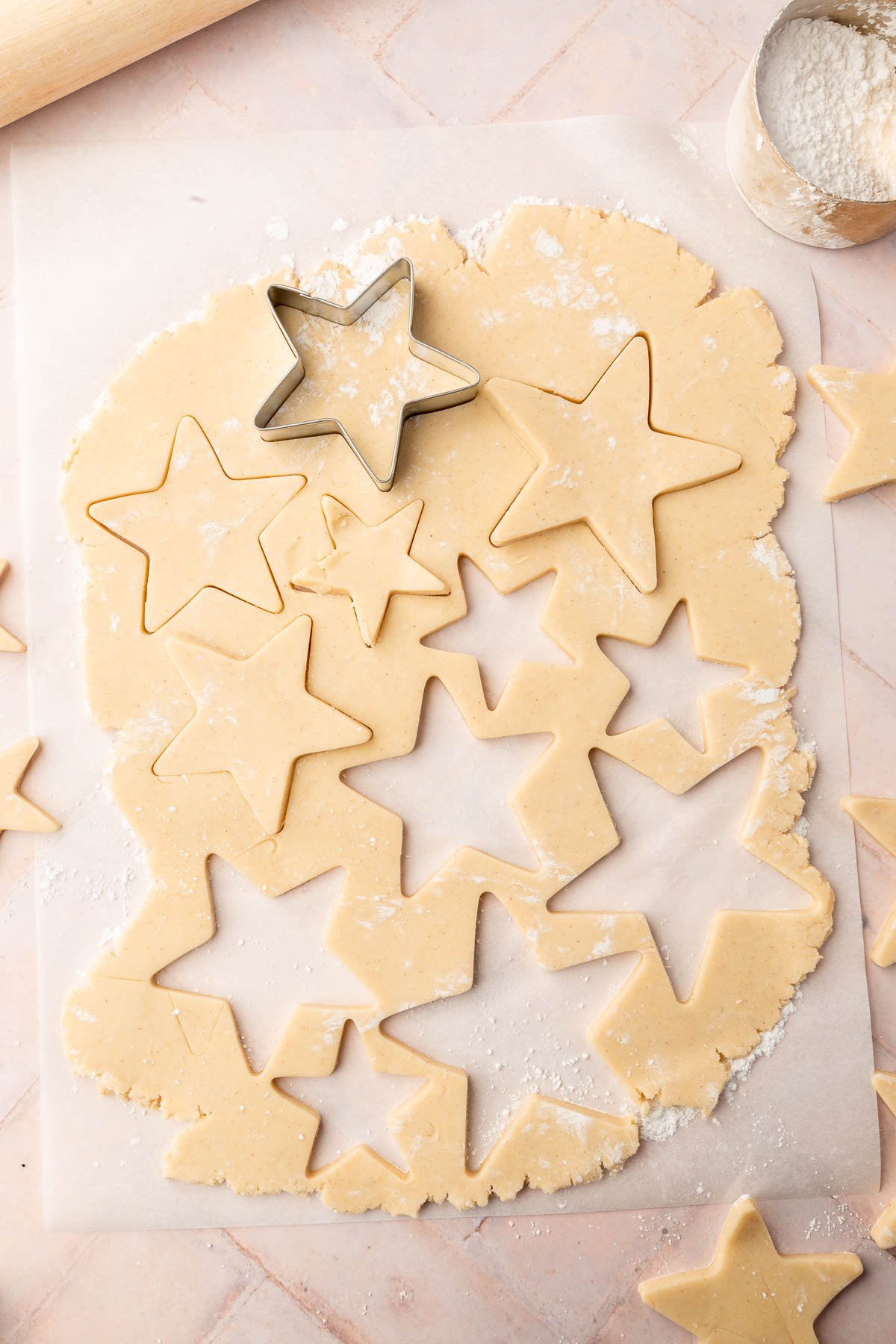 An overhead view of rolled out gluten free sugar cookie dough on a piece of parchment paper with several stars cut out of it with star shaped cookie cutters.