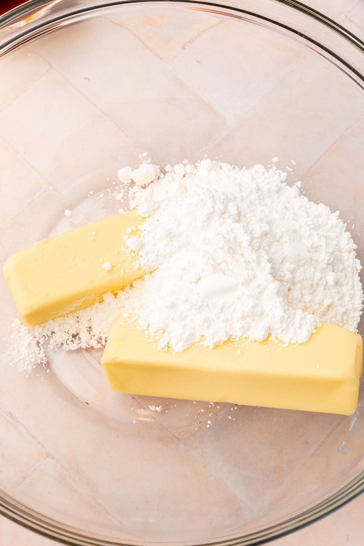 Two sticks of butter and powdered sugar in a glass mixing bowl.