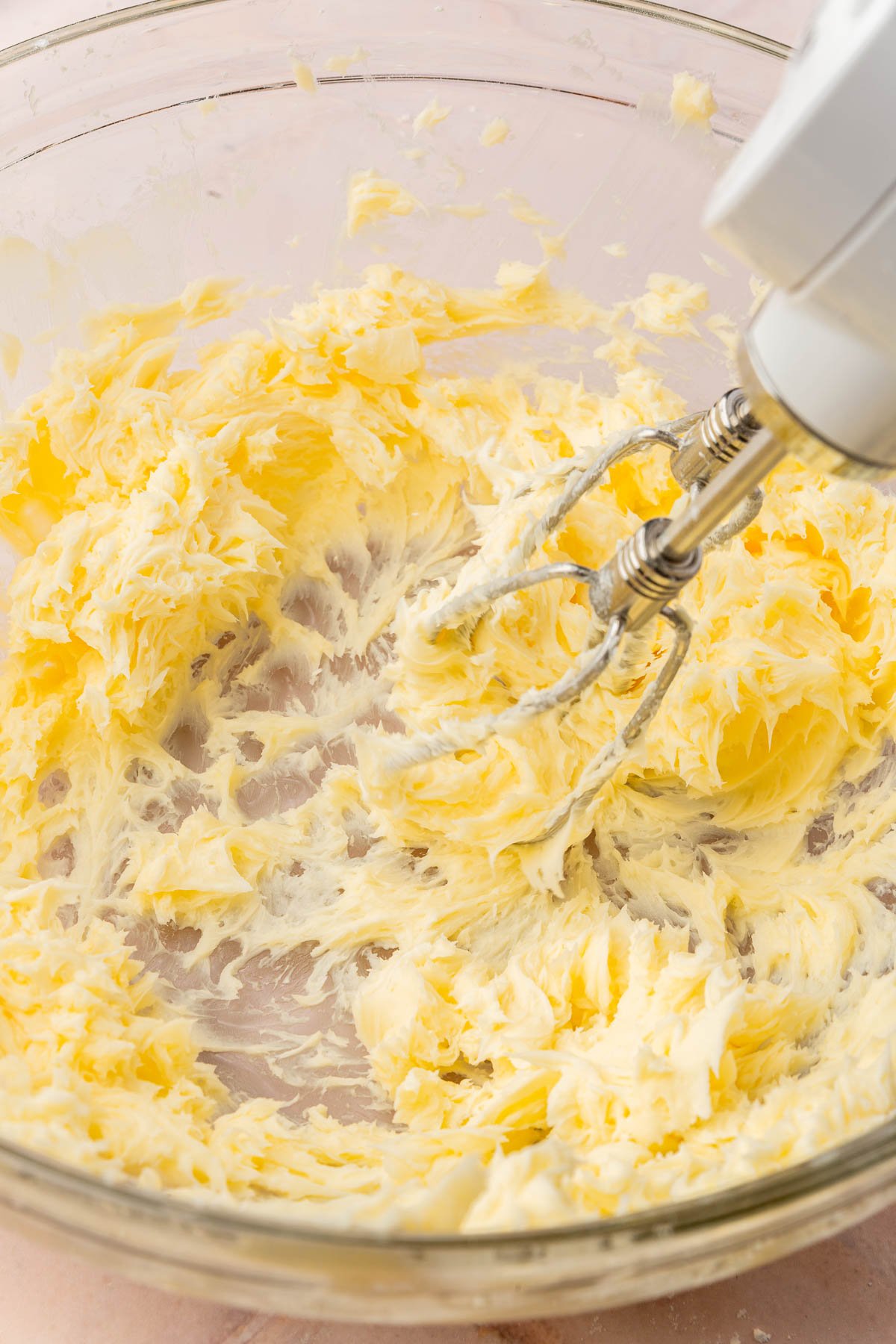 Butter and powdered sugar being creamed together with an electric mixer in a large glass mixing bowl.