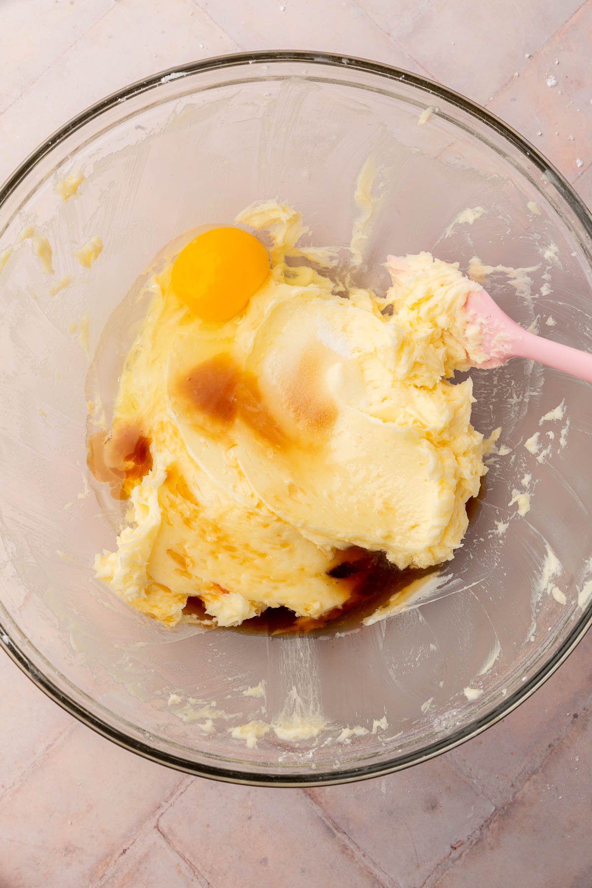 An overhead view of creamed butter and powdered sugar topped with eggs, vanilla and salt in a glass mixing bowl.