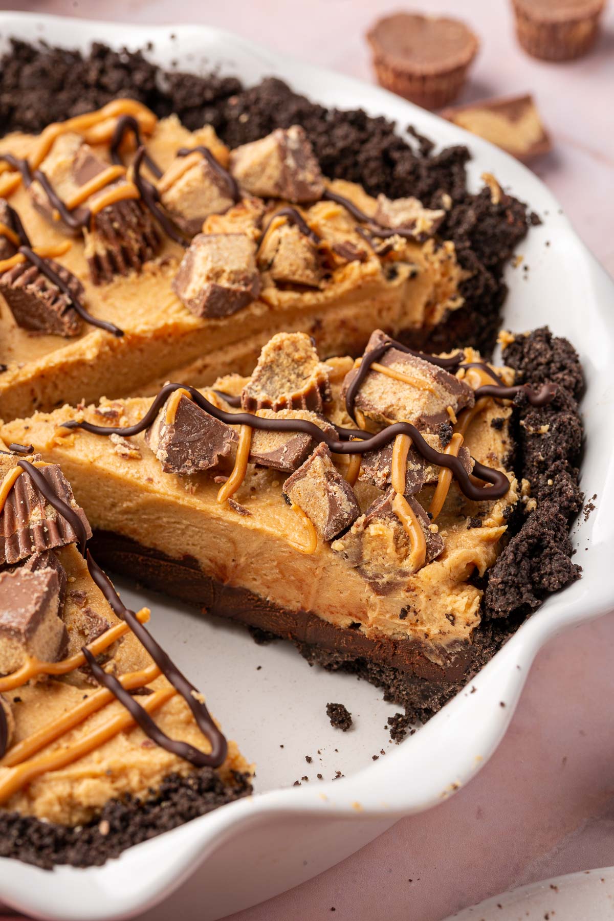 Slices of gluten-free Oreo peanut butter pie topped with reese's peanut butter cups in a pie plate.