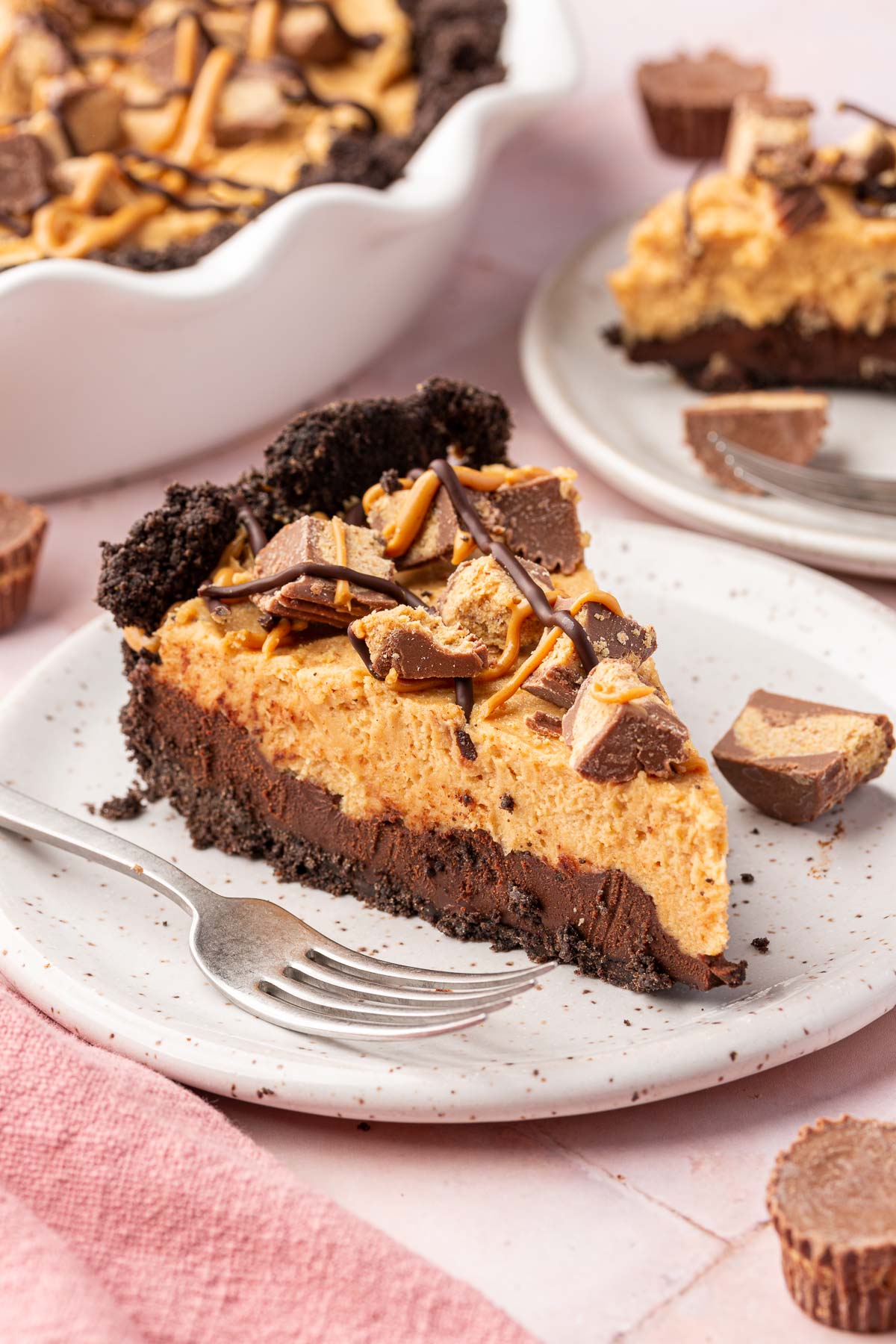 A single slice of Oreo peanut butter pie with chocolate ganache and reese's peanut butter cups on a plate with a fork.