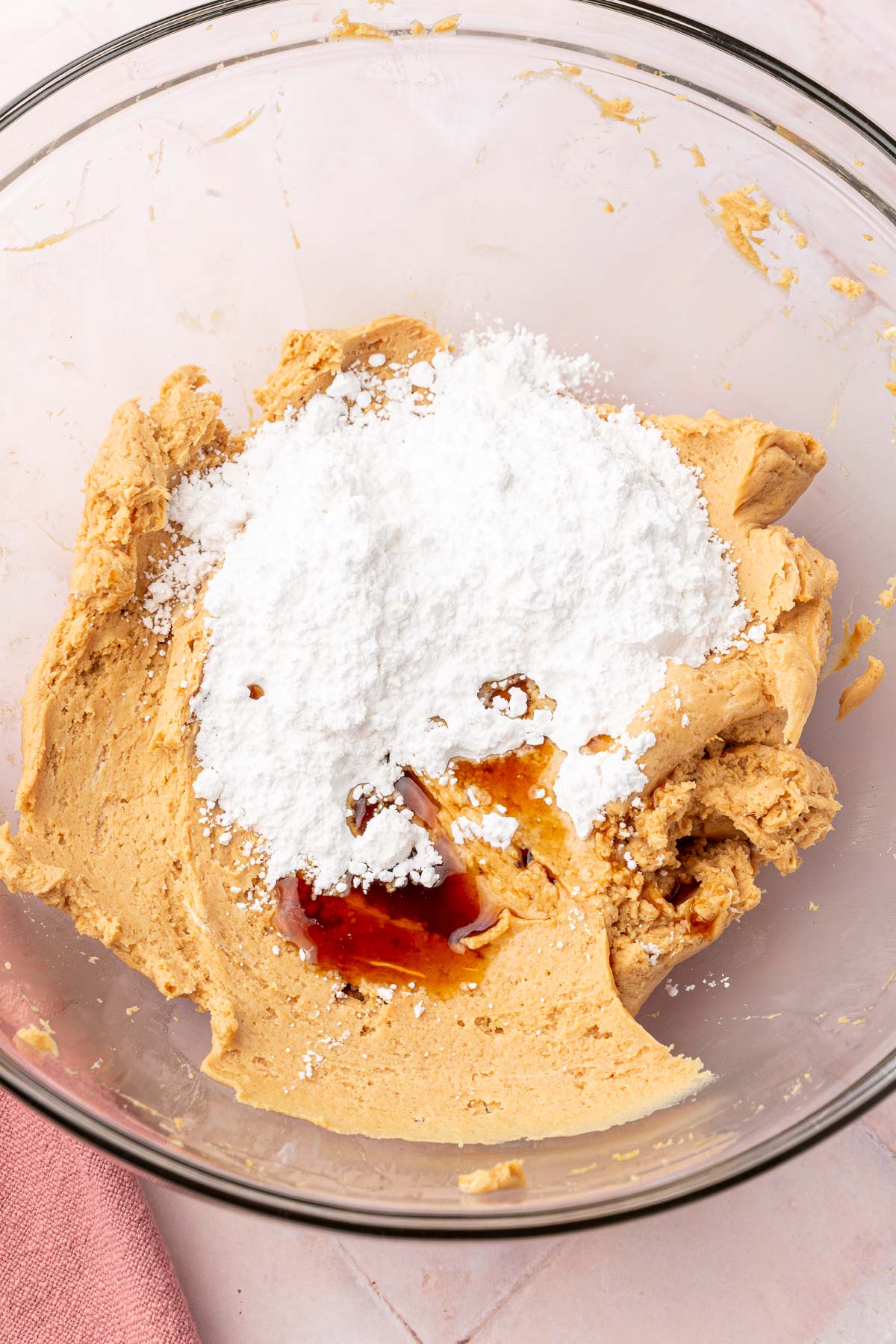 A glass mixing bowl with a peanut butter cream cheese mixture topped with powdered sugar and vanilla extract.
