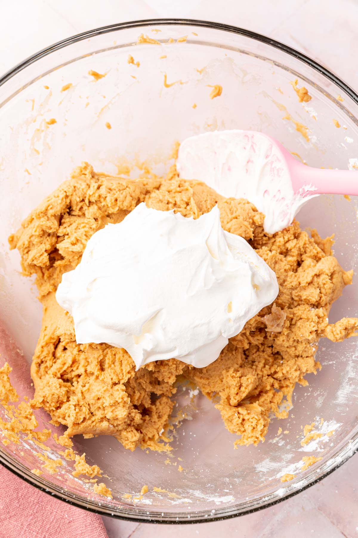 A glass mixing bowl with a peanut butter cream cheese filling topped with a mound of Cool whip before folding together.