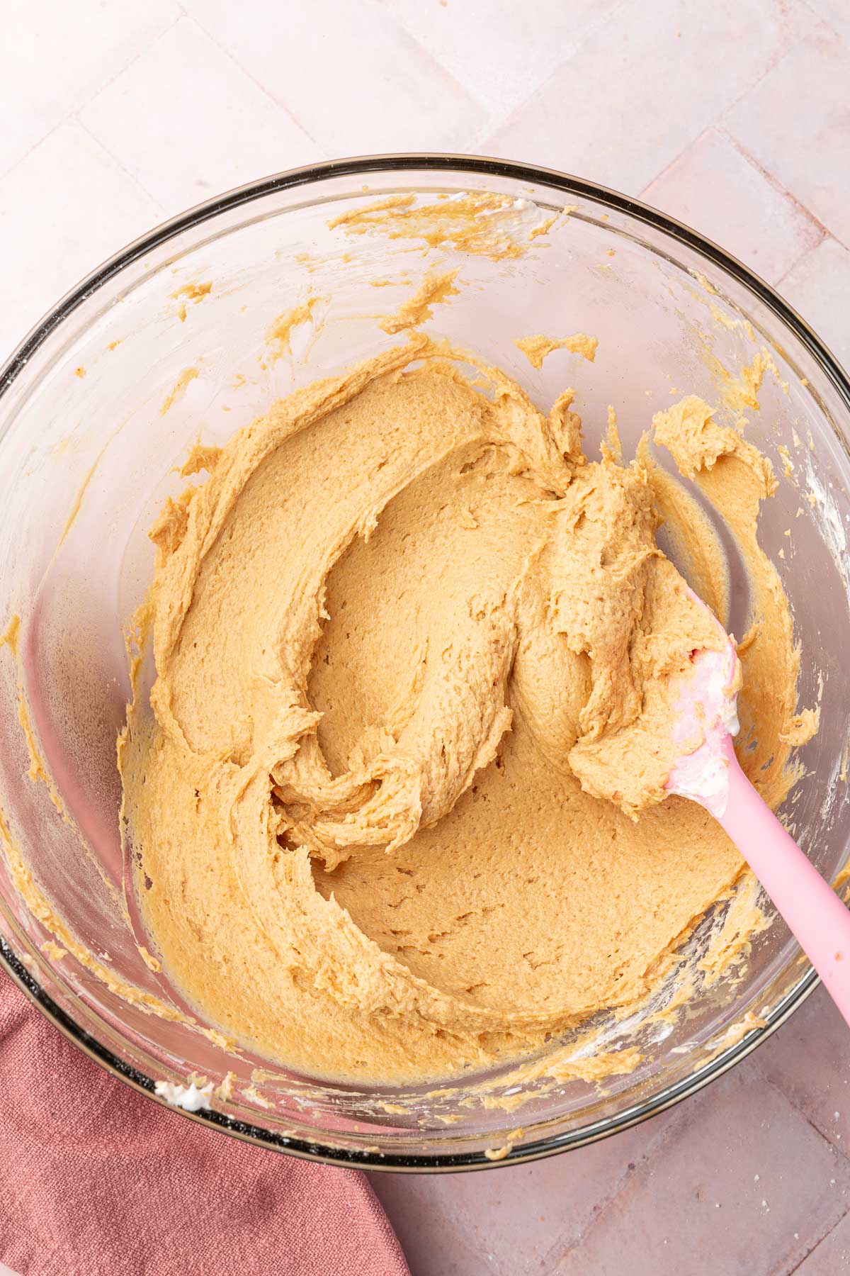 A glass mixing bowl with a fluffy peanut butter cream cheese filling in it with a pink spatula.
