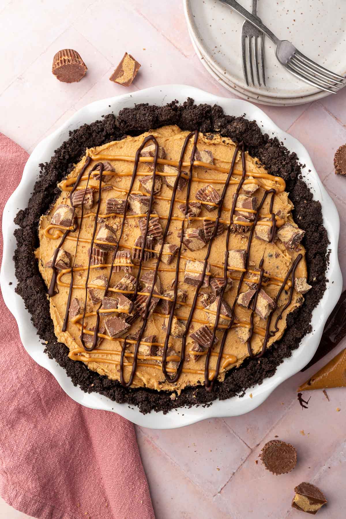 An overhead view of an Oreo peanut butter pie topped with reese's peanut butter cups and drizzles of chocolate and peanut butter.