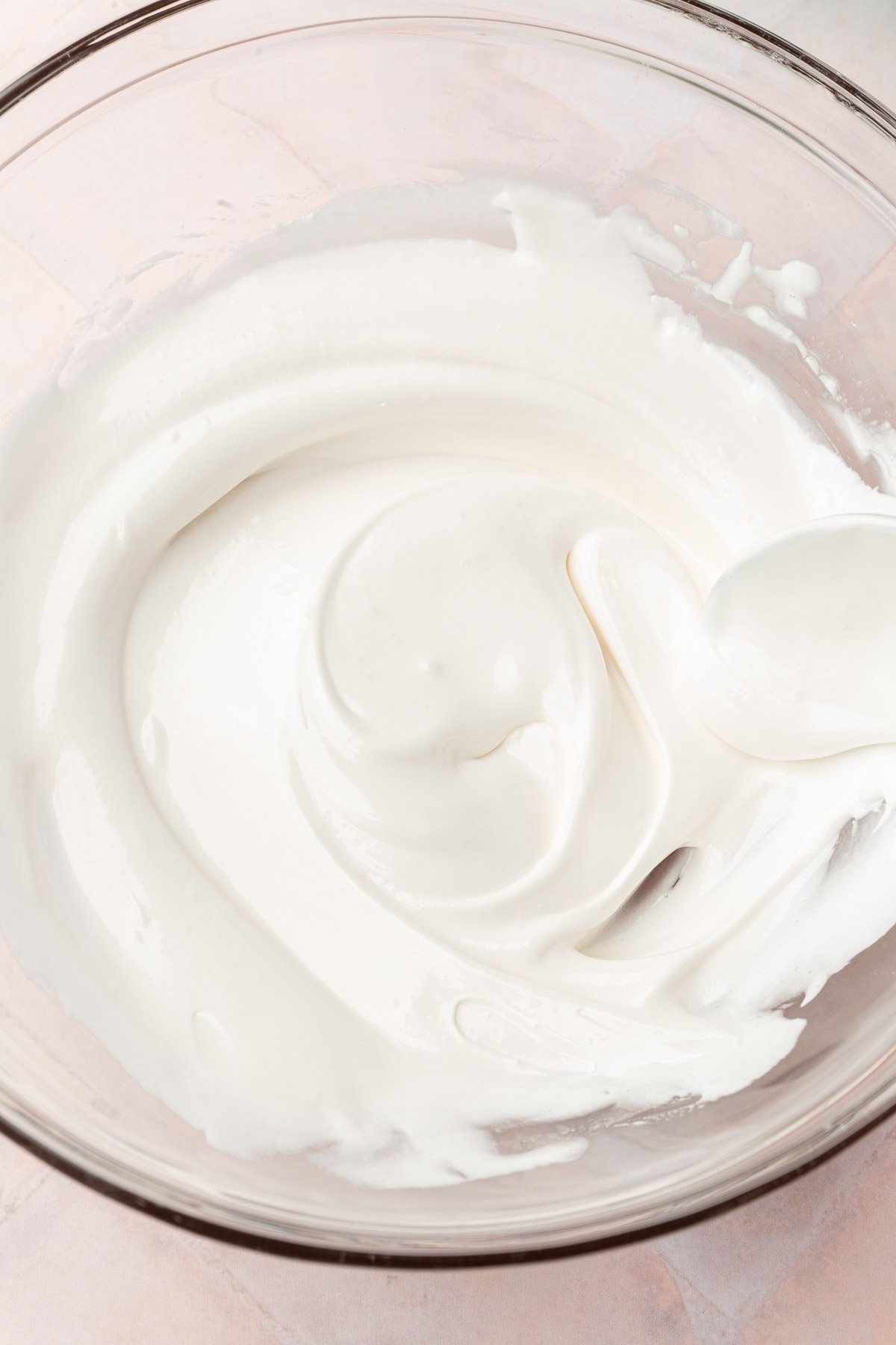 A glass mixing bowl with thinned out white royal icing in it with a spoon.