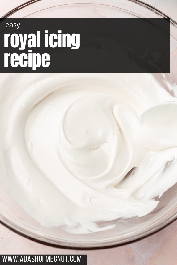 A glass mixing bowl with thinned out white royal icing in it with a spoon.