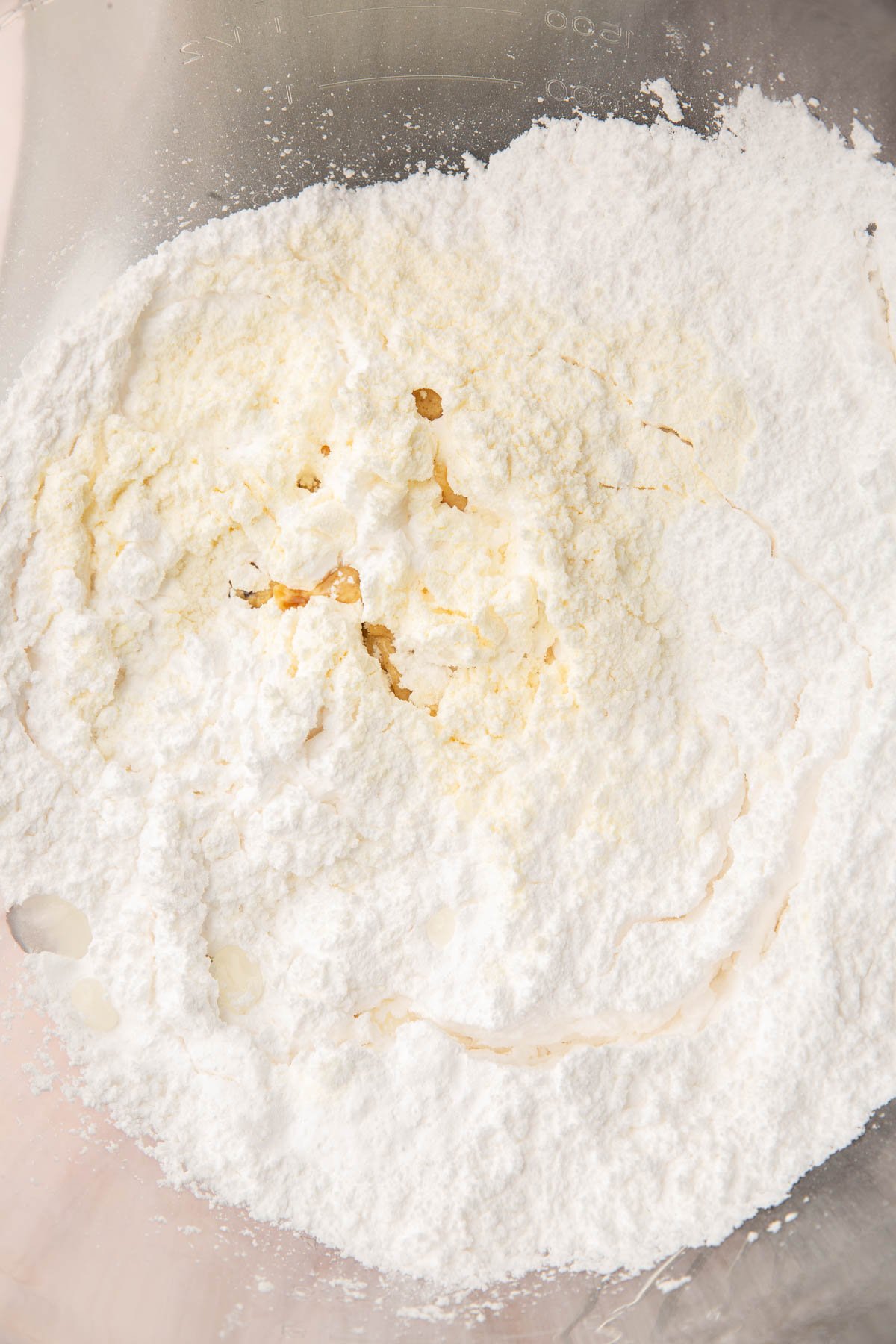 A glass mixing bowl with powdered sugar, vanilla, water, and meringue powder before mixing together.