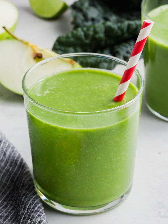 A glass of apple kale smoothie with a red striped straw.