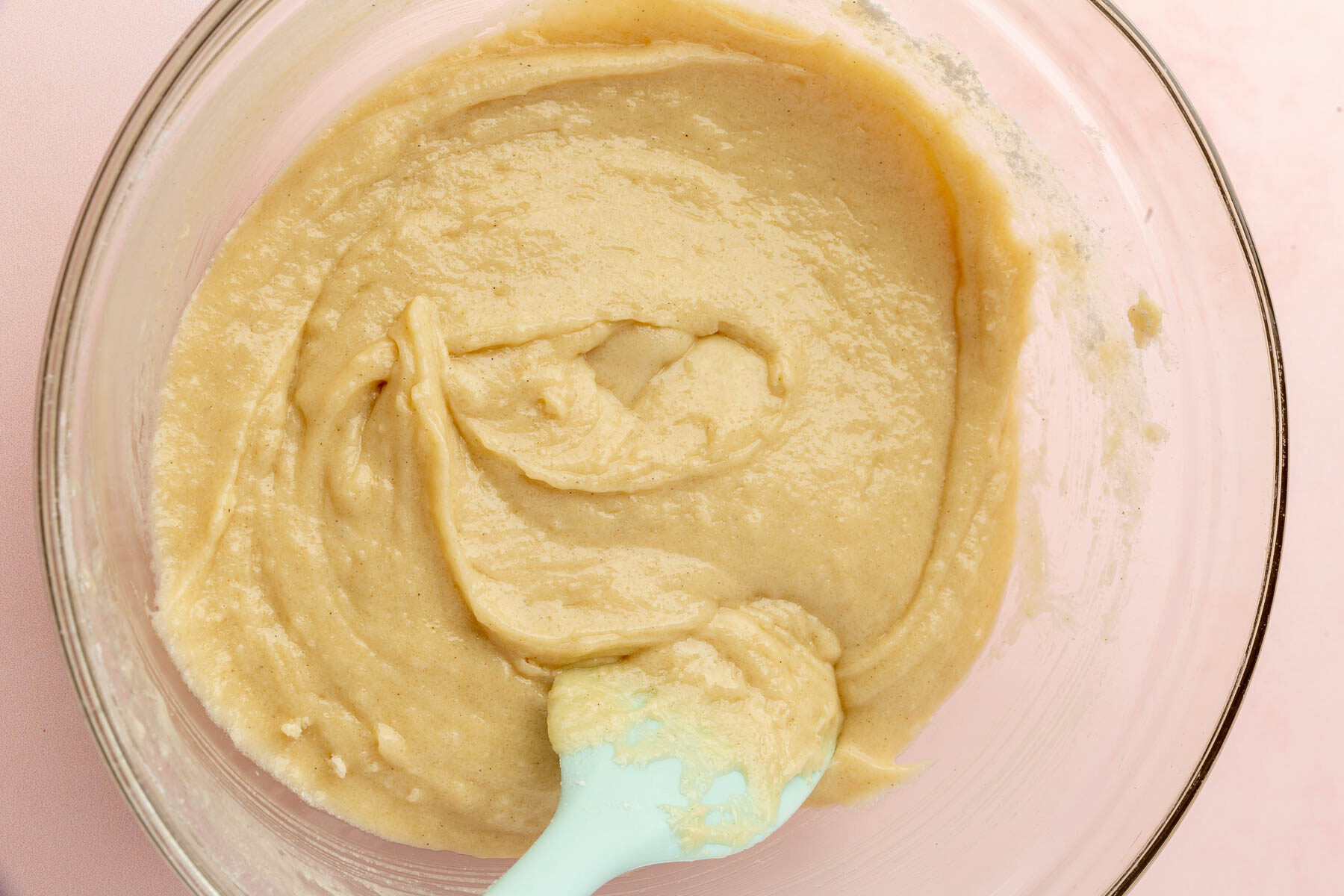 A glass mixing bowl with gluten-free muffin batter and a blue rubber spatula in it.
