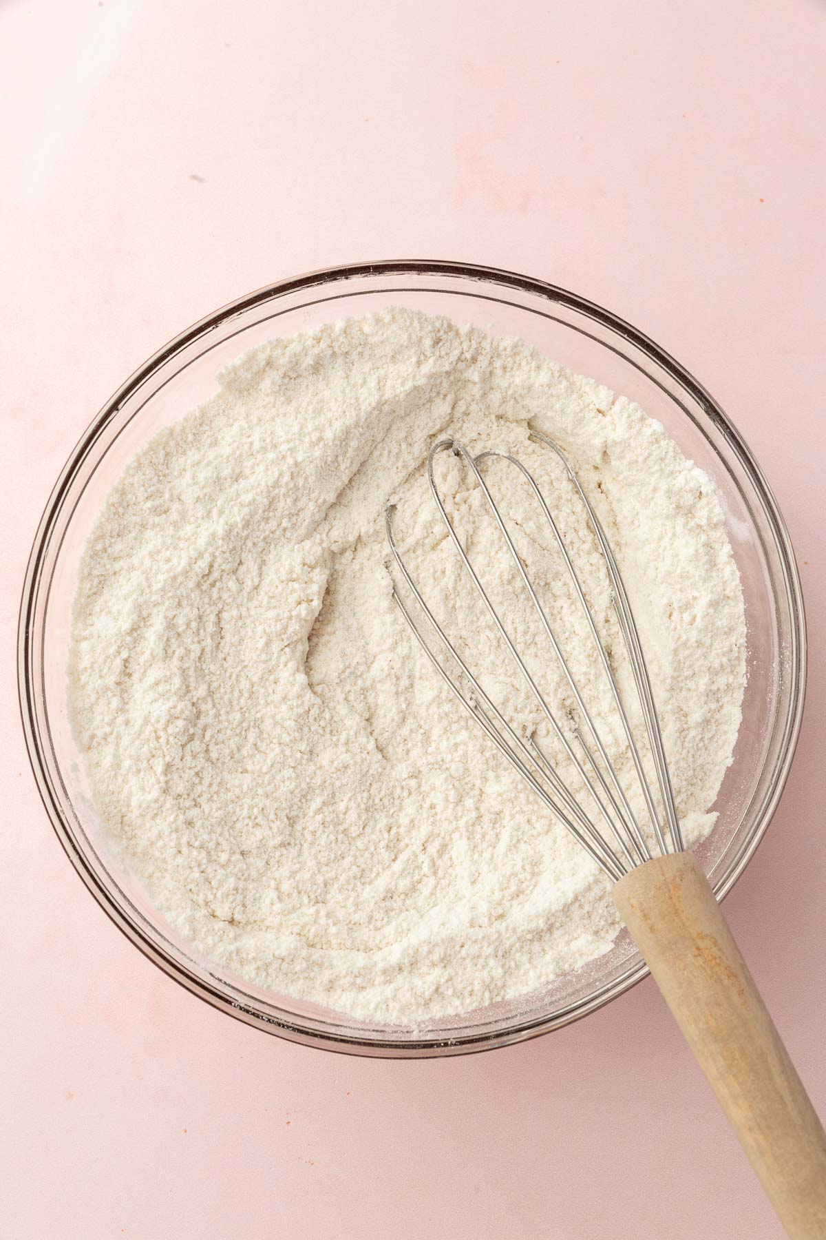 A glass mixing bowl of gluten-free flour blend with a whisk.