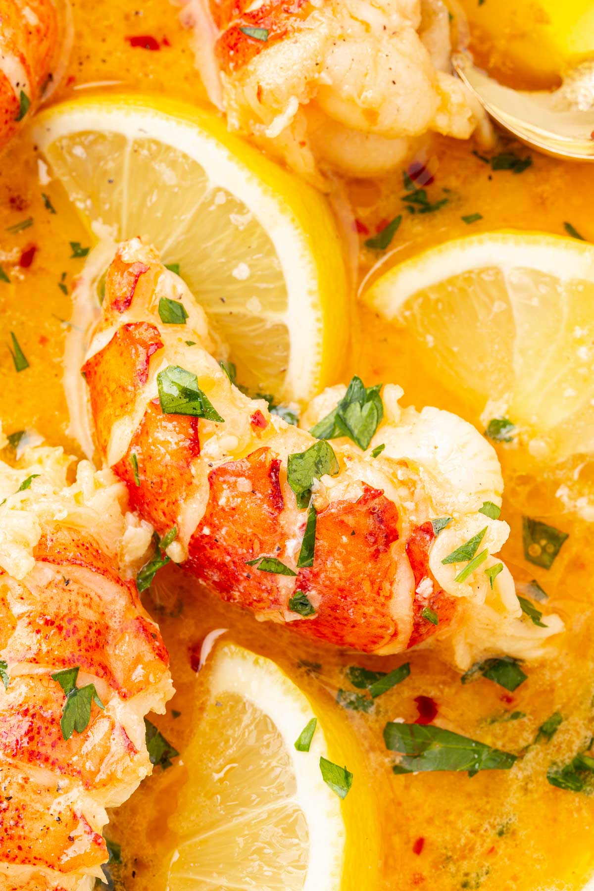 An overhead view of butter poached lobster in a butter garlic sauce with fresh parsley and lemon wedges.