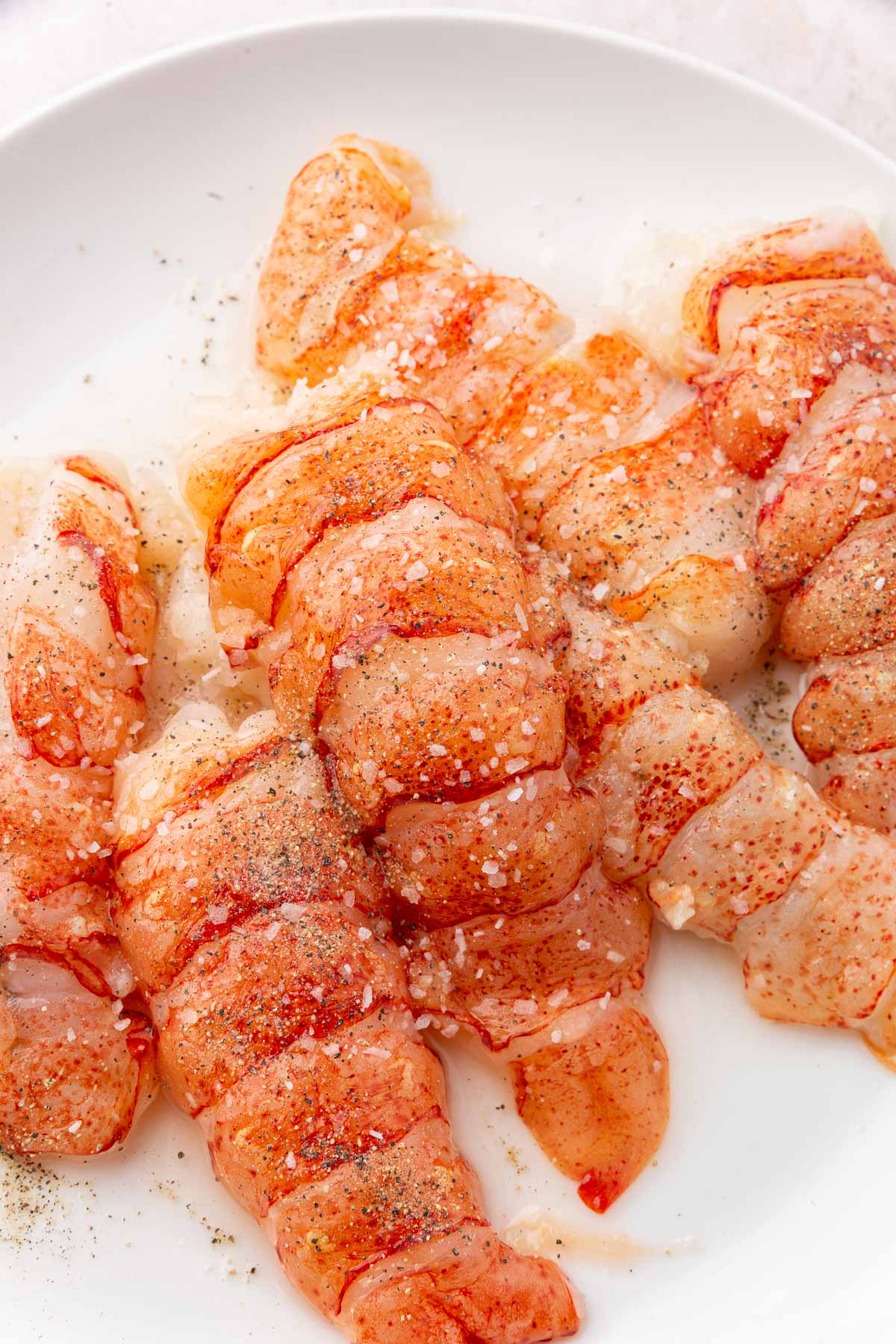 Raw lobster tails on a plate seasoned with salt and pepper.