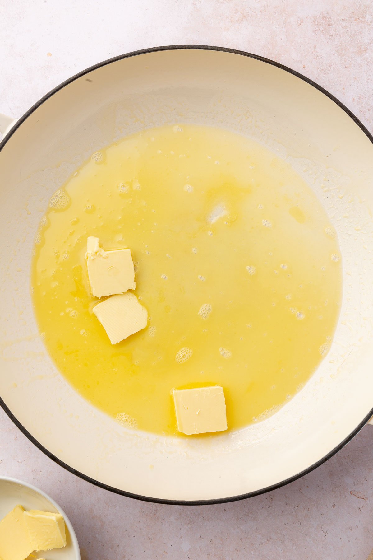 A braising pan with three tablespoons of butter that are partially melted.