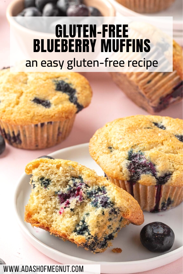 A gluten free blueberry muffin cut in half on a small plate with additional muffins and fresh blueberries in the background.