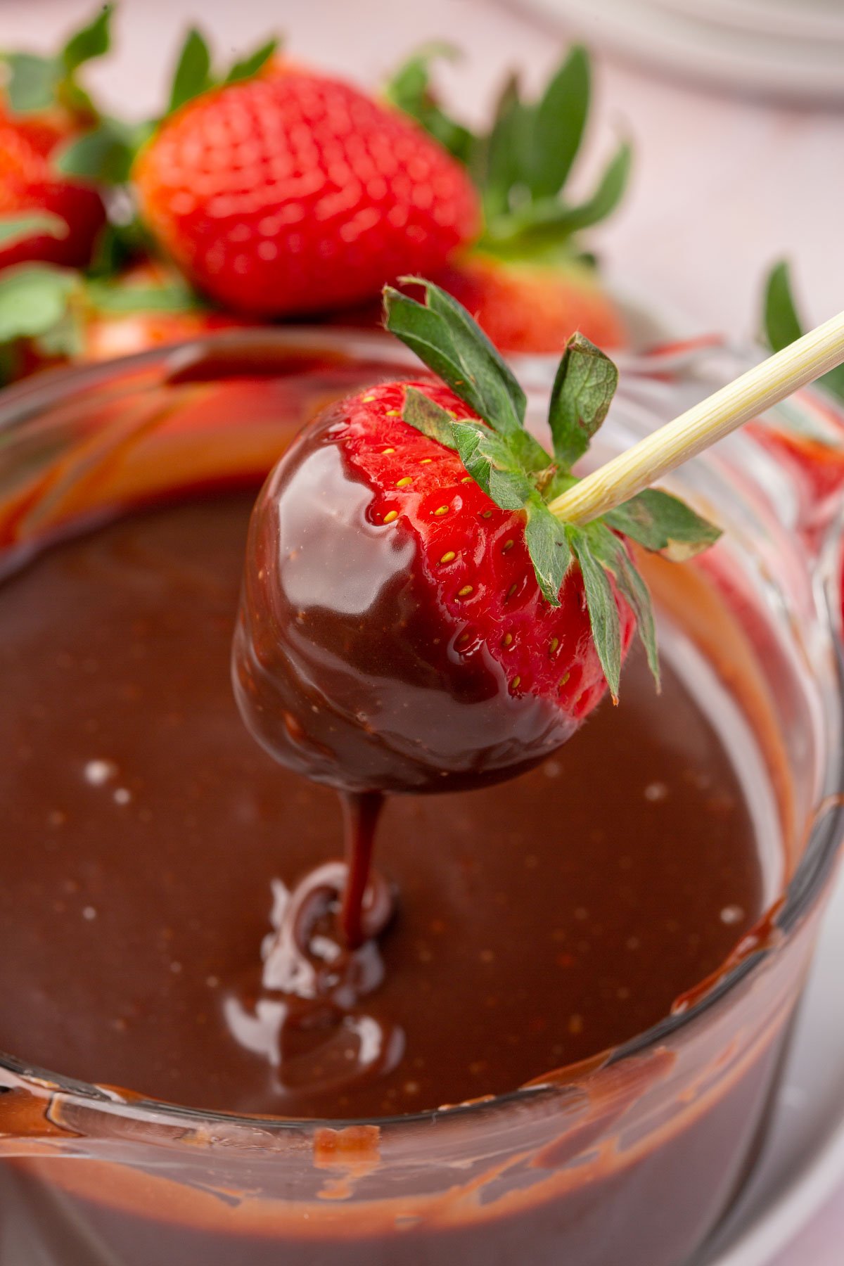 A strawberry on a wooden skewer that has been dipped into Nutella ganache over a bowl of more ganache.