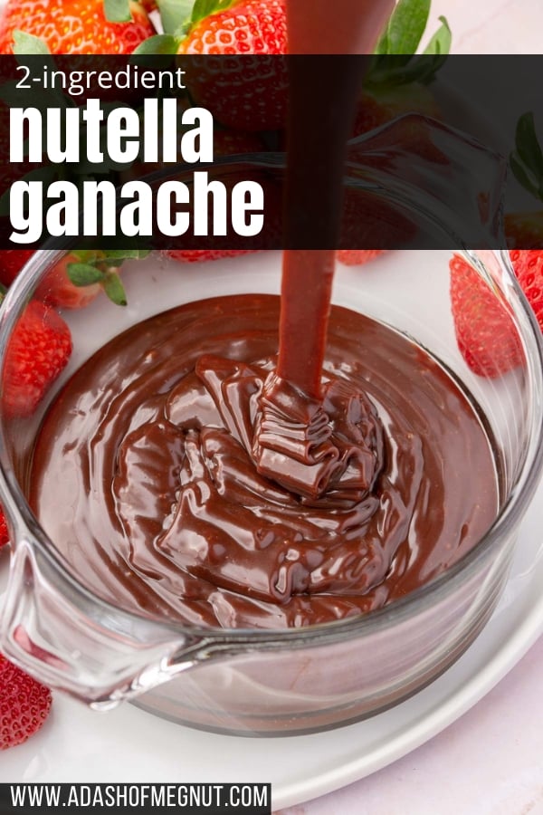 Nutella ganache being drizzled into a glass ramekin on a plate of fresh strawberries.