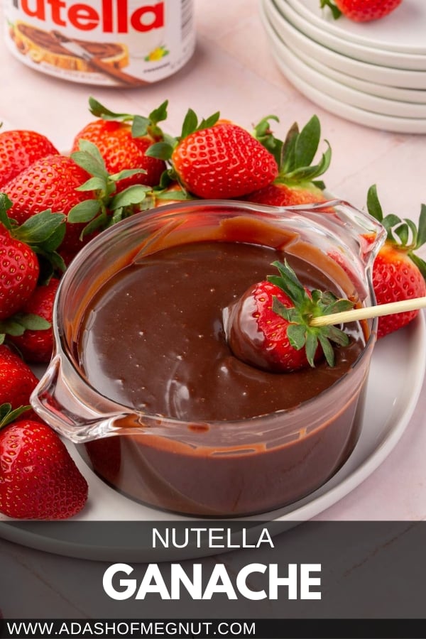 A ramekin of nutella ganache with a skewered strawberry dipped into it on a plate of whole strawberries with a pink linen napkin next to it.